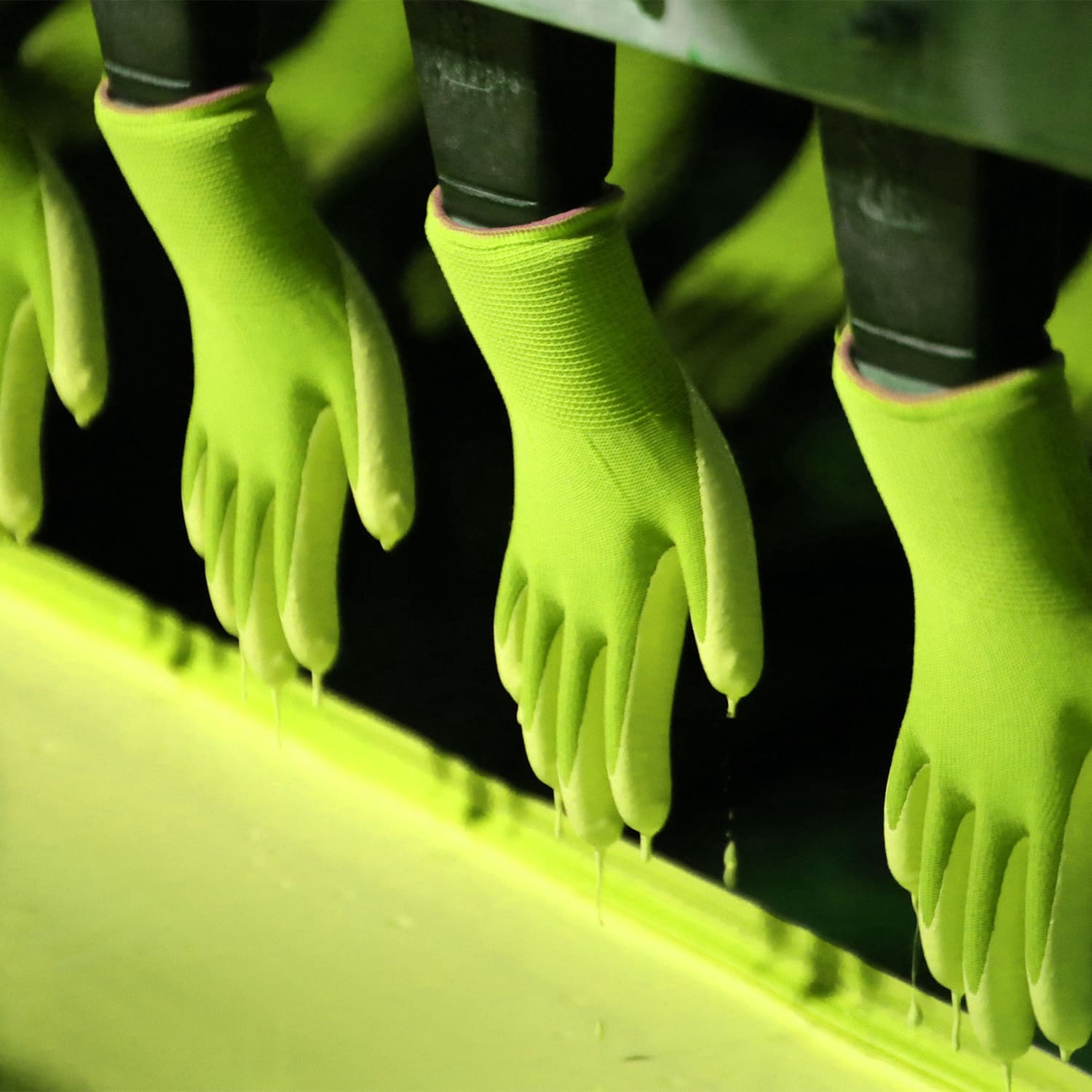 Bright green safety gloves on black mannequin hands, dripping with coating during manufacturing process