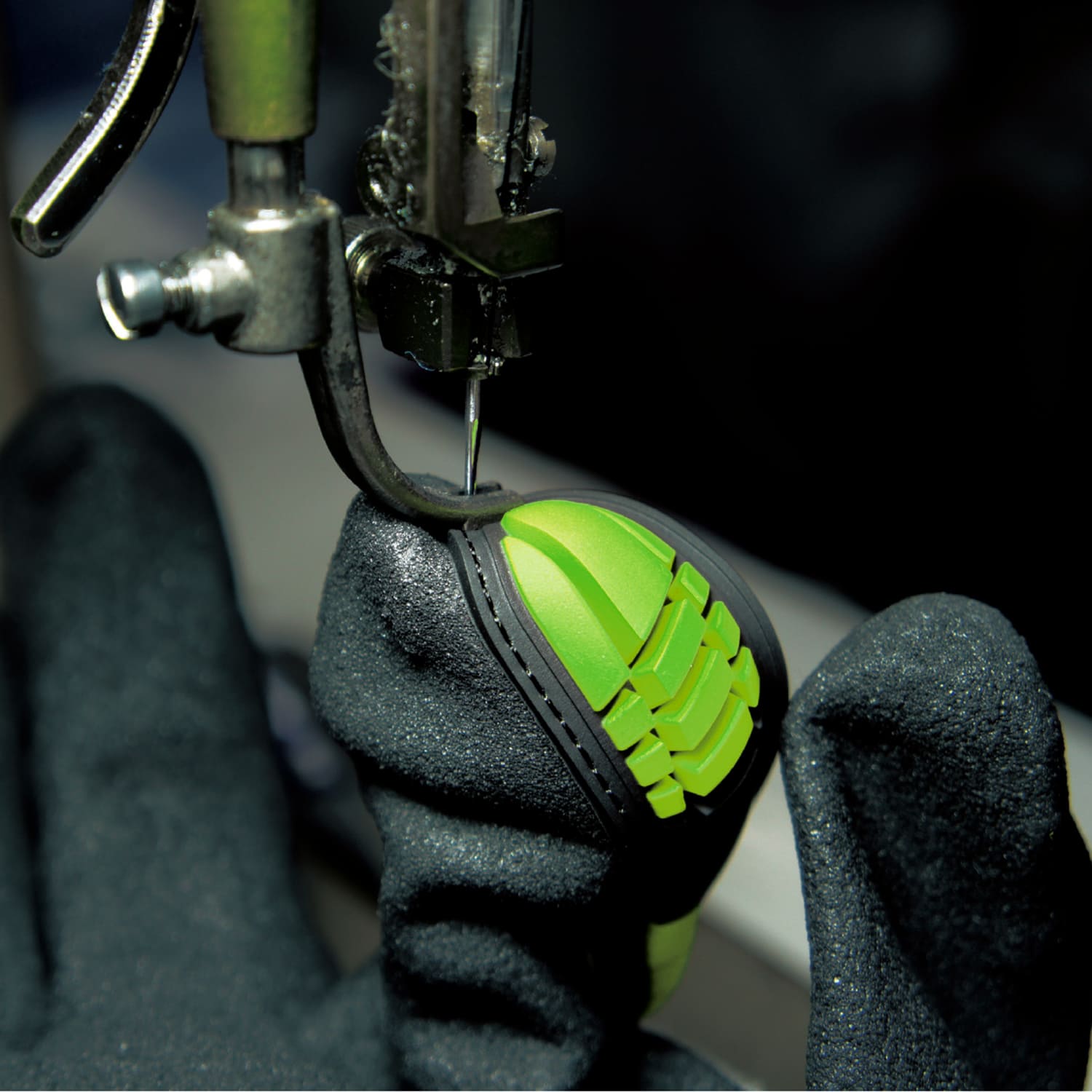 Black safety glove with green grip being tested for puncture resistance in industrial setting